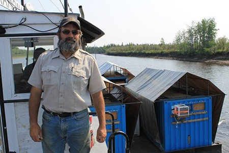 Bruning on the Yukon River on a barge summer 2015 transporting wood bison bulls to the Lower YukonInnoko River herd Bison are inside the custom blue container on the right with an airconditioner and tarp helping keep them cool enroute