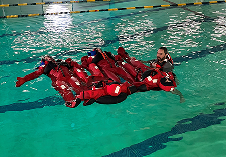 Fish and Game staff engage in pool exercises wearing PFDs and as shown here immersion or survivial suits Exercises include how to right and enter a life raft and how to stay together in an open water scenario