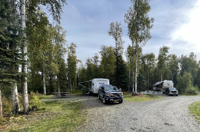 Truck pulling an RV at a campground surrounded by trees