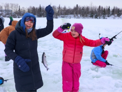 A woman and a younger girl holding up a fish they caught while ice fishing on a lake
