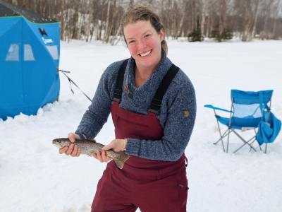 A woman proudly holding a fish she caught while ice fishing on a lake