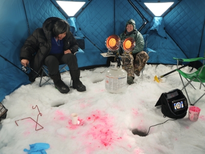 Two women inside an ice fishing hut waiting for fish to bite their lines