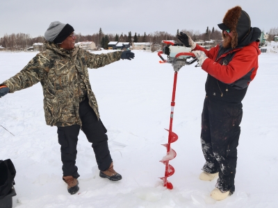 A woman happy she learned how to drill an ice fishing hole next to a man holding the drill